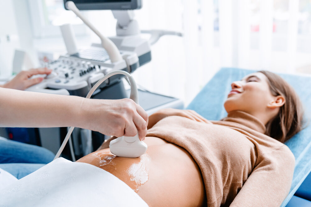 AdobeStock_304536515 (1) A healthcare professional performs an abdominal ultrasound on a pregnant woman lying on an examination table.
