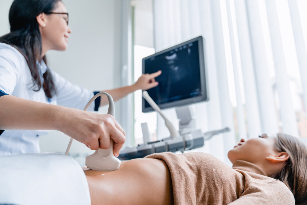 AdobeStock_304536639 (1) Young woman receiving an ultrasound from a female medical staff member wearing a white medical coat.