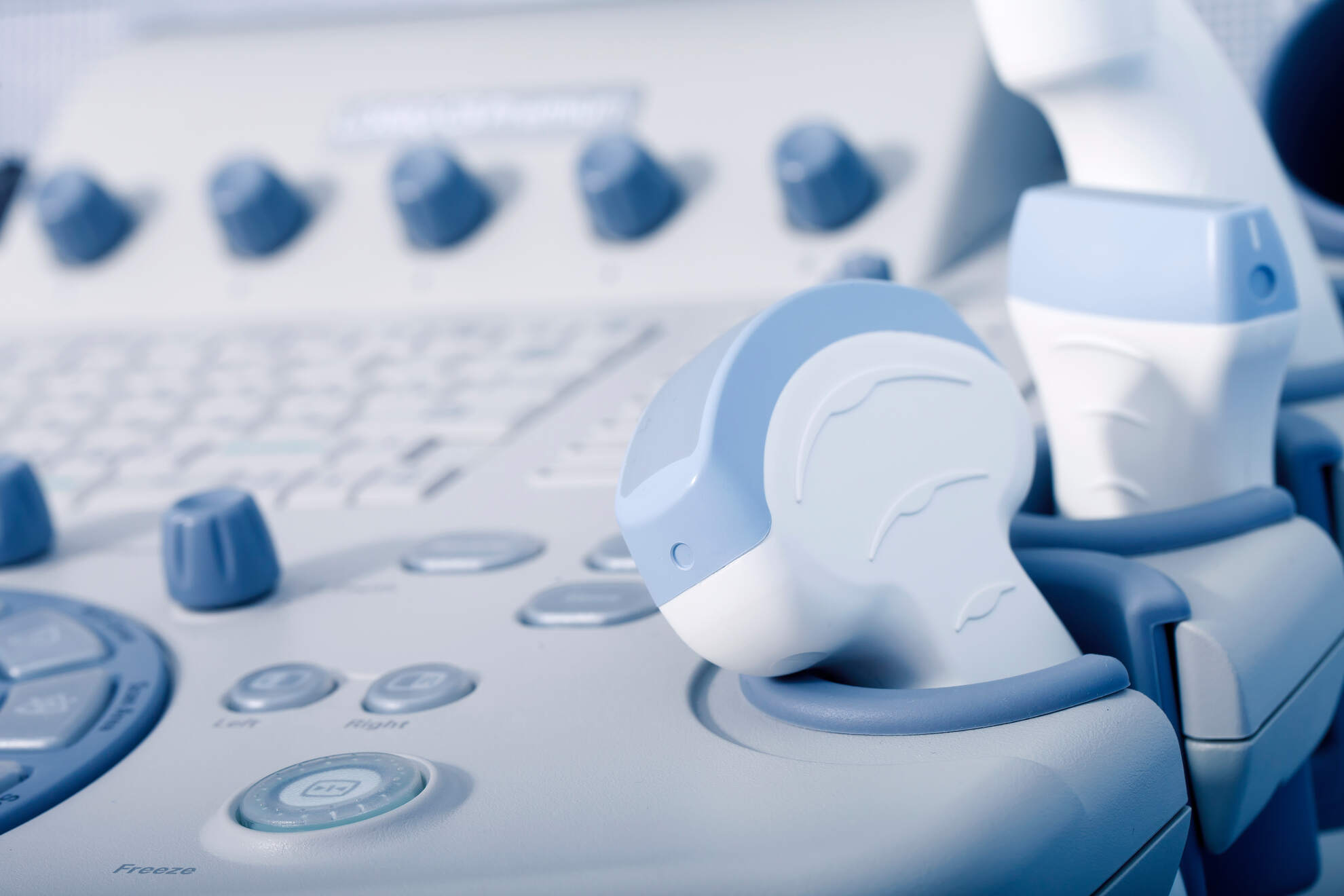 AdobeStock_94839391 (1) Close-up of a modern ultrasound machine control panel with various buttons, dials, and a handheld transducer probe.